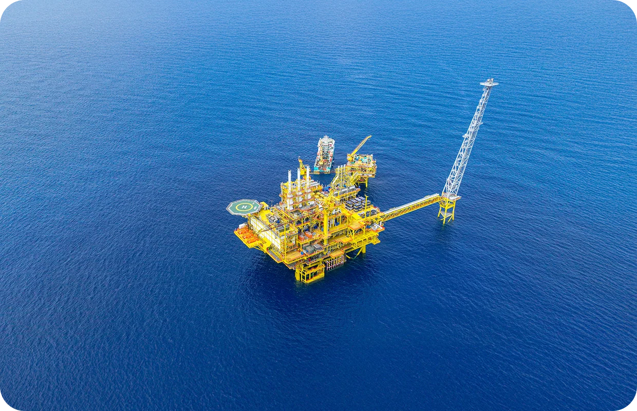 Aerial view of the Kasawari offshore platform: a multi-level yellow structure with a long metal flare boom, a helipad, and a support vessel.
